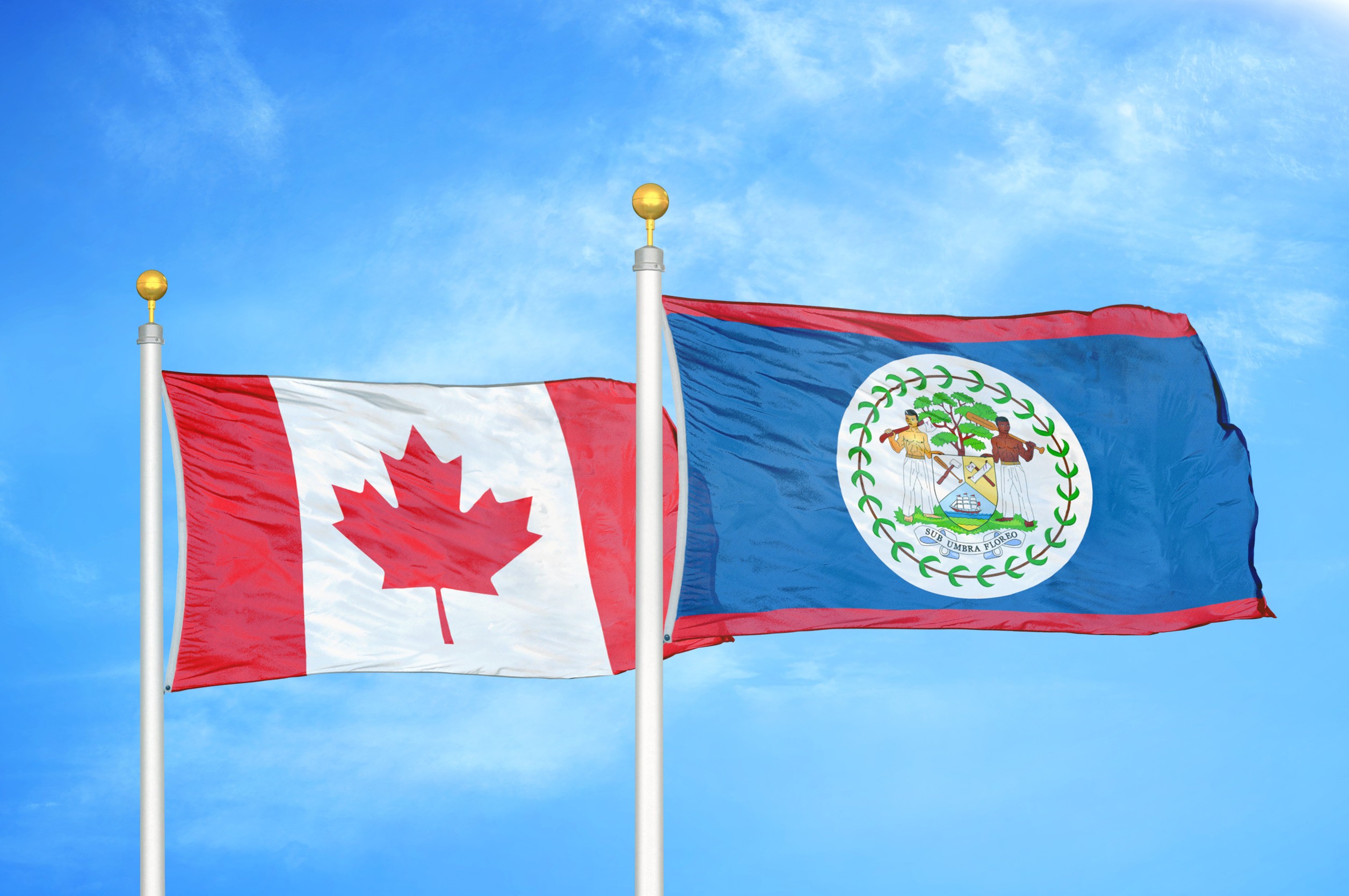 Canada And Belize Two Flags On Flagpoles And Blue Cloudy Sky Background