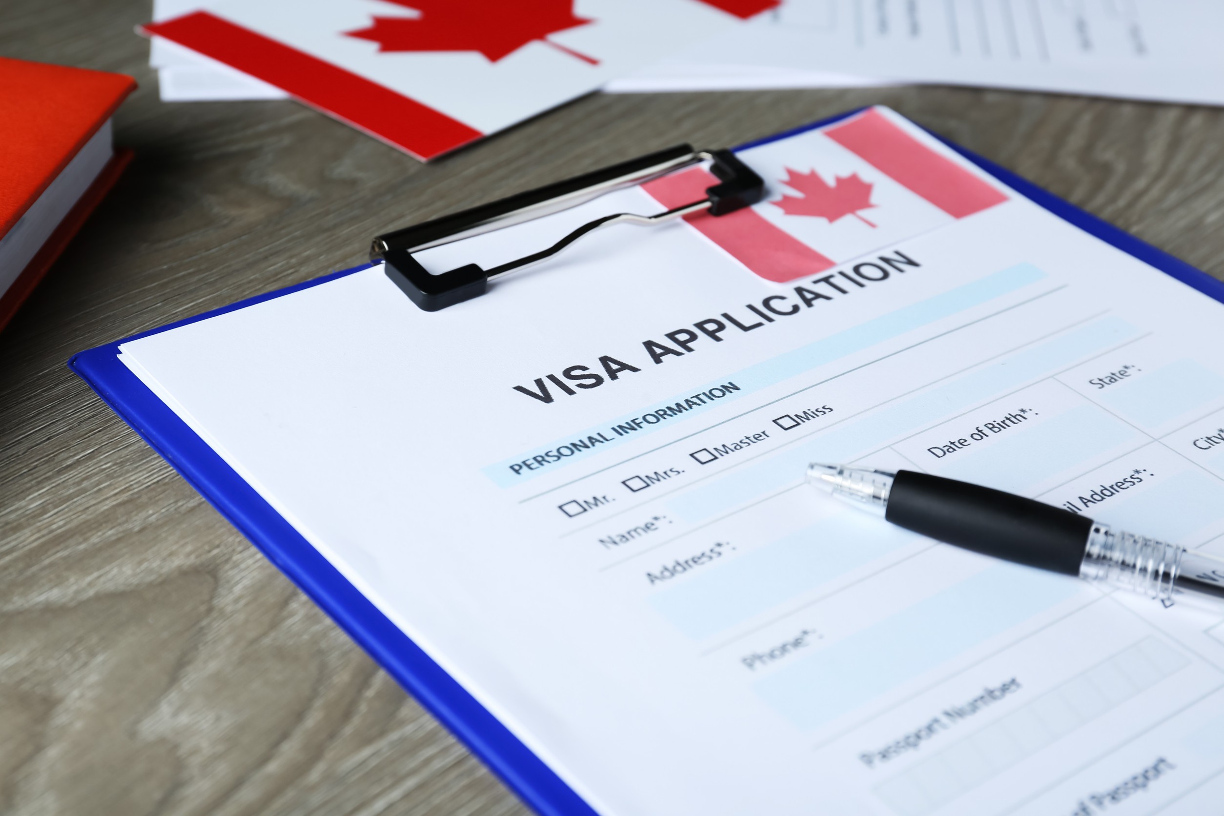 visa application form for immigration to canada and pen on wooden table